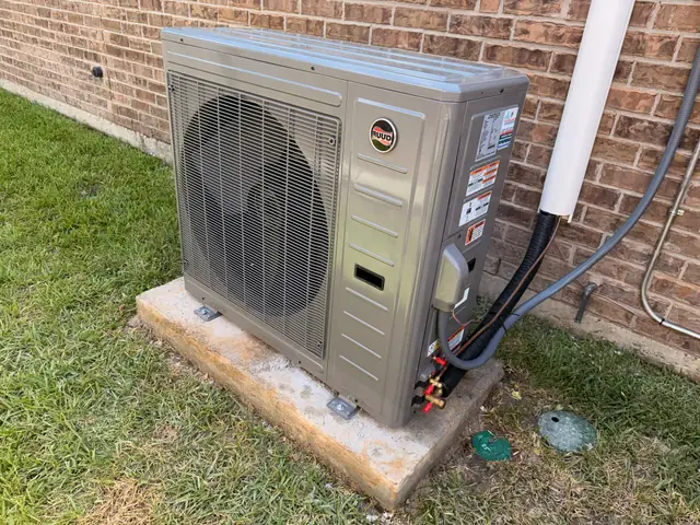 A RUUD condenser installed on a new pad against the brick wall of a Woodlands home